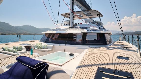 The foredeck of the catamaran featuring a hot tub and cozy seating, surrounded by sea and mountains.