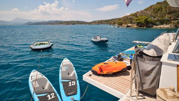 Two paddleboards, a seabob, and an inflatable boat on the catamaran’s deck near the coast.