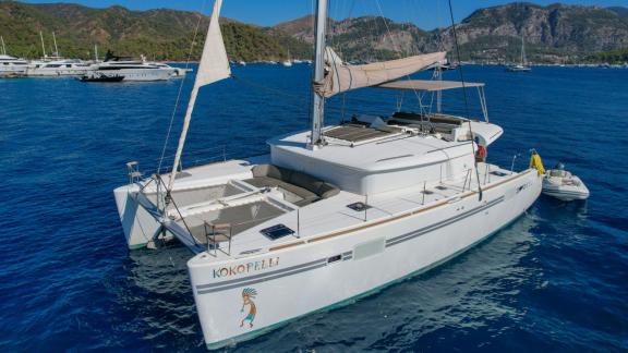 Katamaran Kokopelli liegt in Göcek vor Anker, mit Bergen und Yachten im Hintergrund.