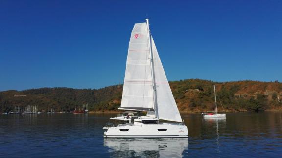 Der Katamaran Lalom segelt in Fethiye, Türkei, auf klarem Wasser, umgeben von grünen Hügeln und einer friedlichen Landsc