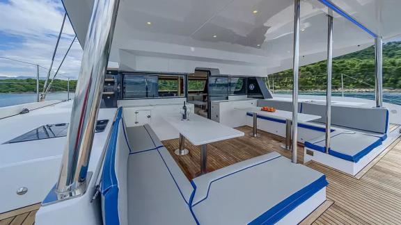 Luna 49 Blue katamaranın arka güvertesinde gölgelikli oturma grubu, yemek masaları ve doğa manzarası yer alıyor.