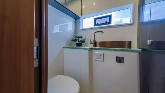 Luna 49 Blue banyosu yeşil tezgah, bakır lavabo ve küçük pencereyle doğal ışık alan modern bir alan sunuyor.