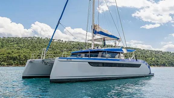 Mavi çizgilere sahip Luna 49 Blue katamaran, Split yakınındaki ormanlık koyda konforlu yat kiralama imkânı sunar.