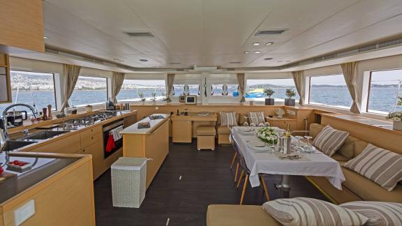 Spacious salon with dining area and kitchen on the Lagoon 560 S2 Meliti, surrounded by large windows with sea views