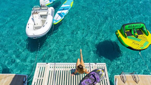 A guest sits at the rear platform. Water toys float in the clear sea.