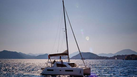 Pata catamaran sailing on the sea with a mountain landscape in the background.