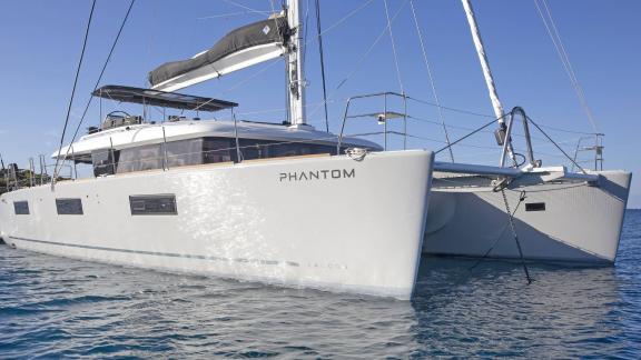 Вид сбоку на катамаран Lagoon 620 Phantom, элегантно стоящий на якоре в воде под голубым небом.