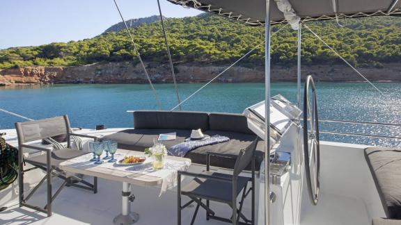 Ormanlık kıyı ve deniz manzaralı, rahat bir şekilde hazırlanmış masalı Lagoon 620 katamaranının flybridge'i.