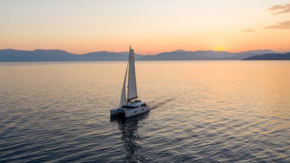 A catamaran sailing peacefully into the sunset on the open sea off the Greek coast.