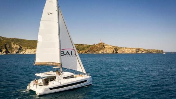 The catamaran Bali 4.2 sails calmly on the blue sea off the rocky coast of Fethiye, Turkey.