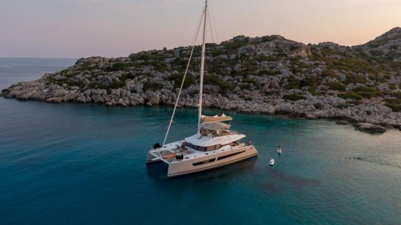 The Serenissima catamaran anchored near a green, rocky coastline.