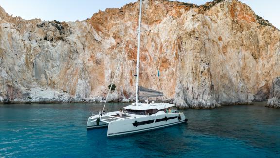 The Serenissima catamaran is calmly anchored in turquoise waters near a massive cliffside.