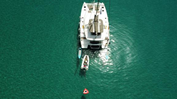 A catamaran with a tender and paddleboard anchored in turquoise, crystal-clear waters.