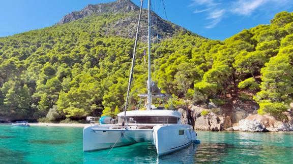 The catamaran Solana is anchored in an idyllic bay in Palairos, surrounded by lush greenery.