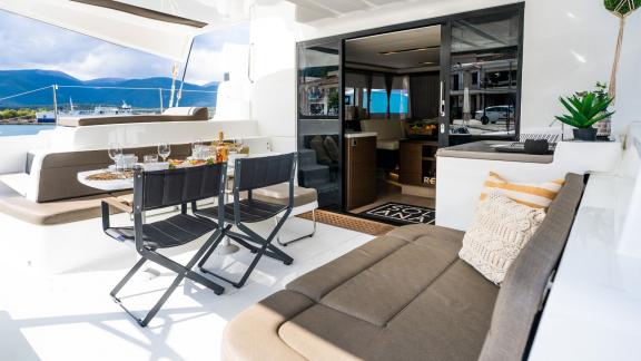 The outdoor area of a catamaran with cozy seating and a set dining table, perfect for alfresco meals.