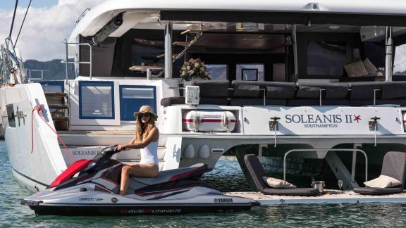 Woman riding a jet ski beside the yacht Soleanis II, positioned near the stern on the water