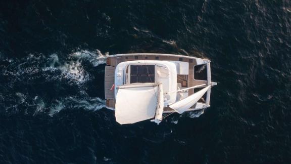 The catamaran Spice of Life sails off Athens, seen from above on deep blue waters.