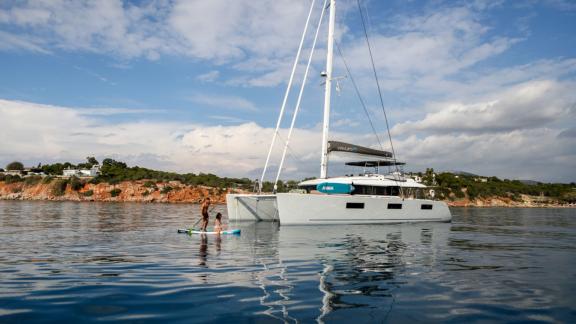 Der Katamaran Valium 62 liegt im ruhigen Meer vor Anker, während Leute auf Paddleboards entspannen.