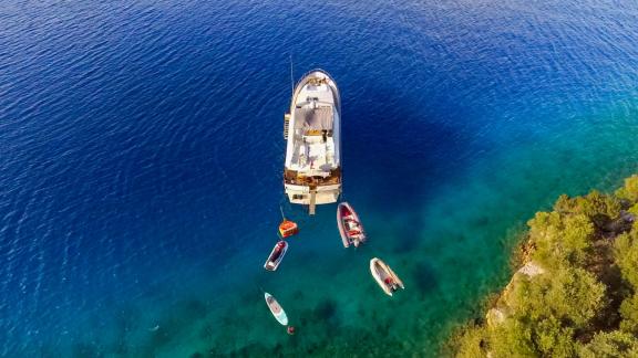 Aus der Vogelperspektive die Motoryacht Samocla, vor Anker an der Küste und von Wasserspielzeug umgeben.