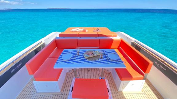 Elegante Sitzecke mit orangefarbenen Polstern auf dem Achterdeck der Motoryacht Ikigai mit Meerblick.