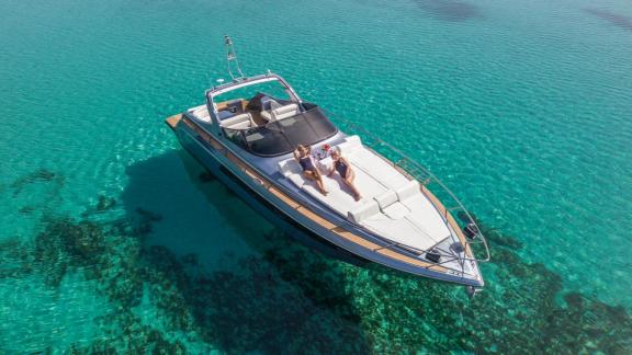 Este motoryatın ön güvertesinde uzanan misafirler, Mykonos’un berrak denizinde güneşin tadını çıkarıyor.