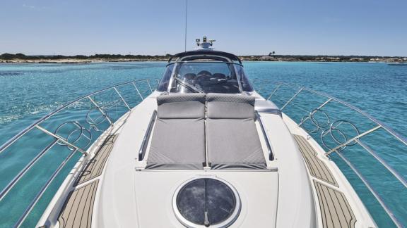 Die Motoryacht Com Tu liegt vor Ibiza vor Anker mit großzügigem Sonnendeck am Bug.