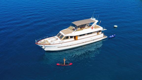 Motor yacht Custom Blanka rests on blue waters, one person paddleboarding.