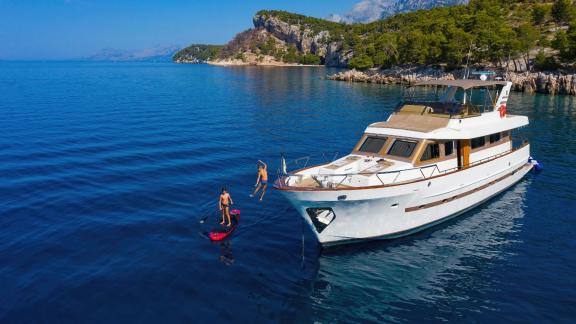 Motor yacht Custom Blanka on blue waters near the shore, people playing with water toys.