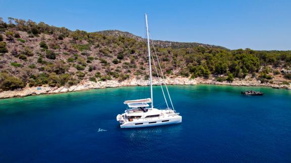 The Catamaran Daiquiri is peacefully anchored in a scenic bay surrounded by mountains with clear blue waters in Greece.