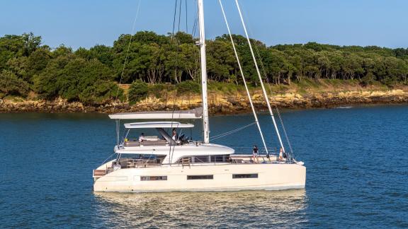 The Catamaran Daiquiri anchored in calm waters near a wooded shoreline in Athens, Greece.