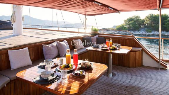 Breakfast table on the deck of the Gulet Cataleya with drinks, food, seating and sea view in the background.