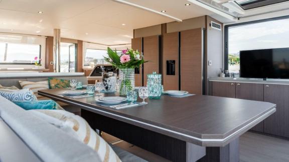 Stylishly set dining table in the cozy interior of a Bali catamaran, with a view of the kitchen.