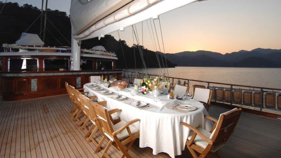 Dining table on yacht deck at sunset with view of calm bay