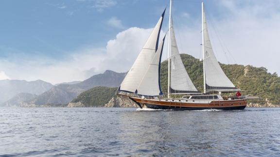 Gulet Diva Deniz with 6 cabins sails off the coast of Marmaris, white sails and green mountains in the background.