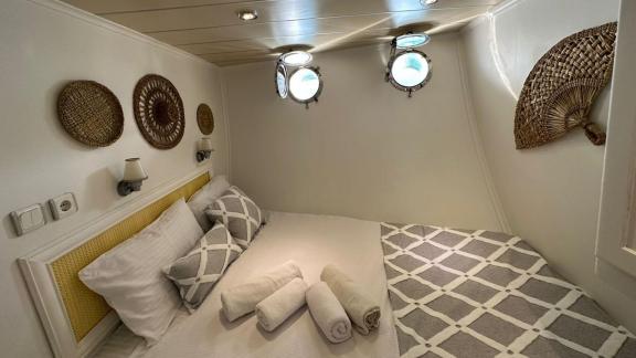 Bright cabin with cozy double bed, decorative baskets, and portholes on Gulet Bohemian in Turkey.