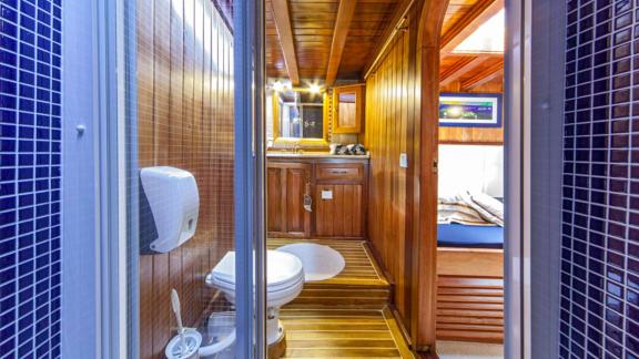 Modern bathroom on a gulet with wooden interior and blue tiles, access to the bedroom.