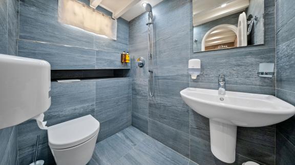 Bad mit modernen grauen Fliesen, Dusche, Waschbecken und WC.