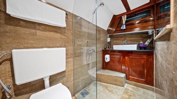 Bad mit Marmoroptik verfügt über Dusche, Waschbecken, WC und Holzschrank.