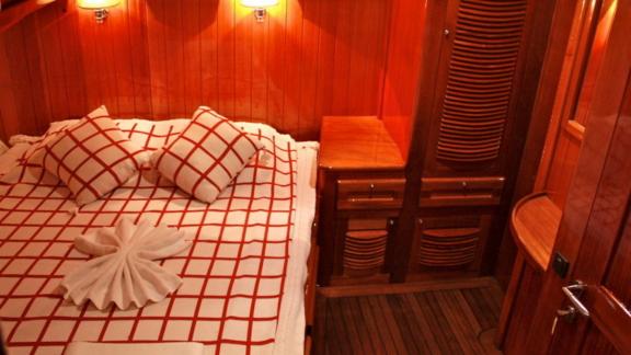 A cozy cabin on Gulet Il Fratello with a double bed, wooden furniture, and warm lighting.