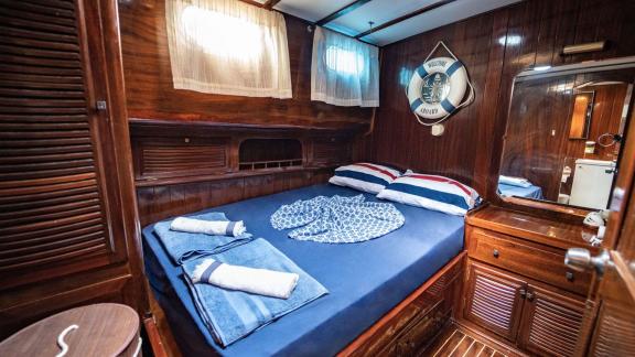 Interior view of a cabin with a double bed, wooden walls, and windows on Gulet Thalasa.