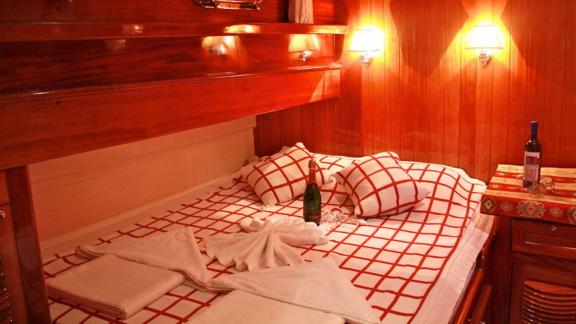 A cozy cabin on Gulet Il Fratello with a double bed, wooden furniture, warm lighting, and a bottle of wine.