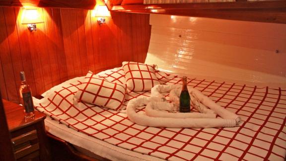 A cozy cabin on Gulet Il Fratello with a double bed, wooden furniture, warm lighting, and a bottle of rosé wine.