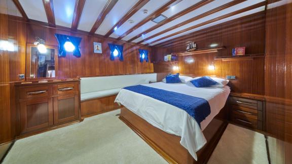 Wood-panelled bedroom on a sailing yacht with a double bed, white and blue duvet covers and a comfortable bench seat