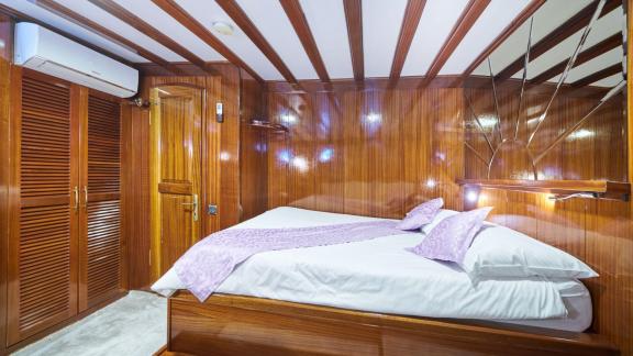 Luxurious cabin on a sailing yacht with wooden walls, a large double bed, purple bed linen and a built-in wardrobe.