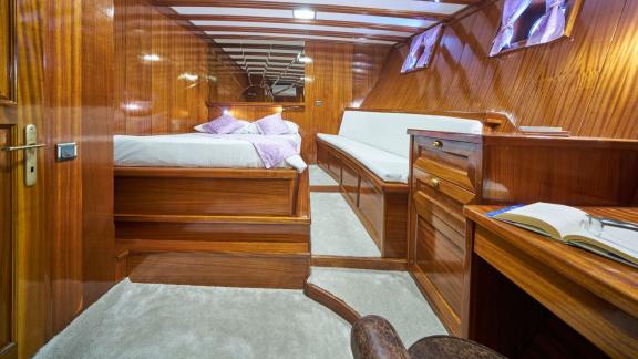 Luxurious cabin on a sailing yacht with wooden walls, raised double bed, purple bed linen, a comfortable bench seat and 