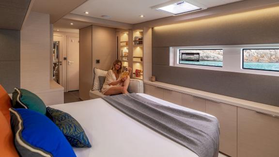 Woman enjoying a book on the sofa in an elegant yacht double cabin with large window and stylish decor.