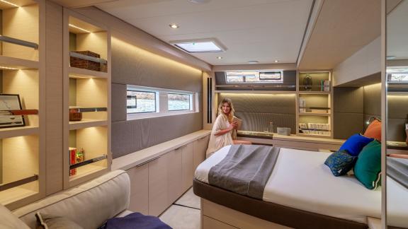 Woman in a bright yacht cabin with stylish shelves, large windows, and elegant decor.