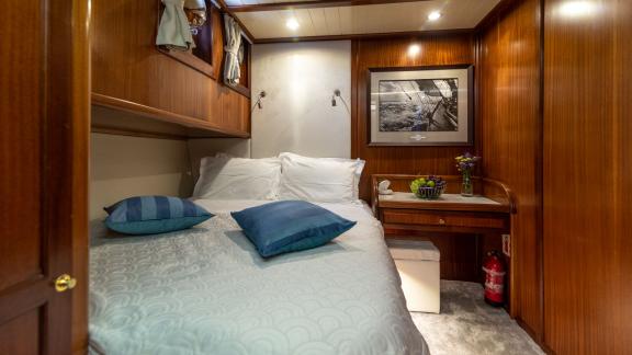 A cosy cabin on board the Gulet Smart Spirit with a comfortable bed, a small desk and stylish wooden furnishings.