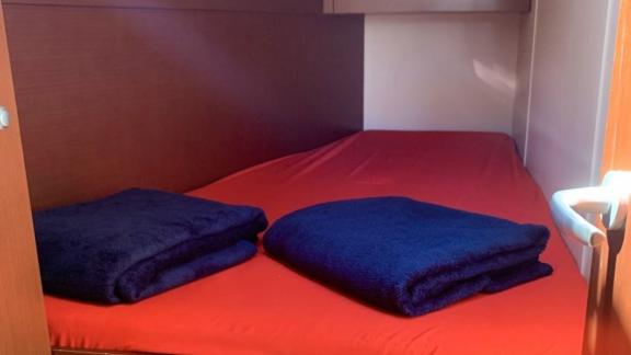 The double cabin of the Deneb sailing yacht features a bed with a red cover and dark blankets.