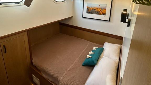 This compact cabin features a comfortable double bed with simple brown linens and a stylish wall picture.